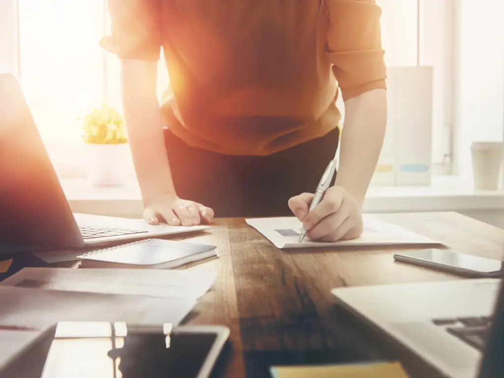 Person writing at desk with sunlight.